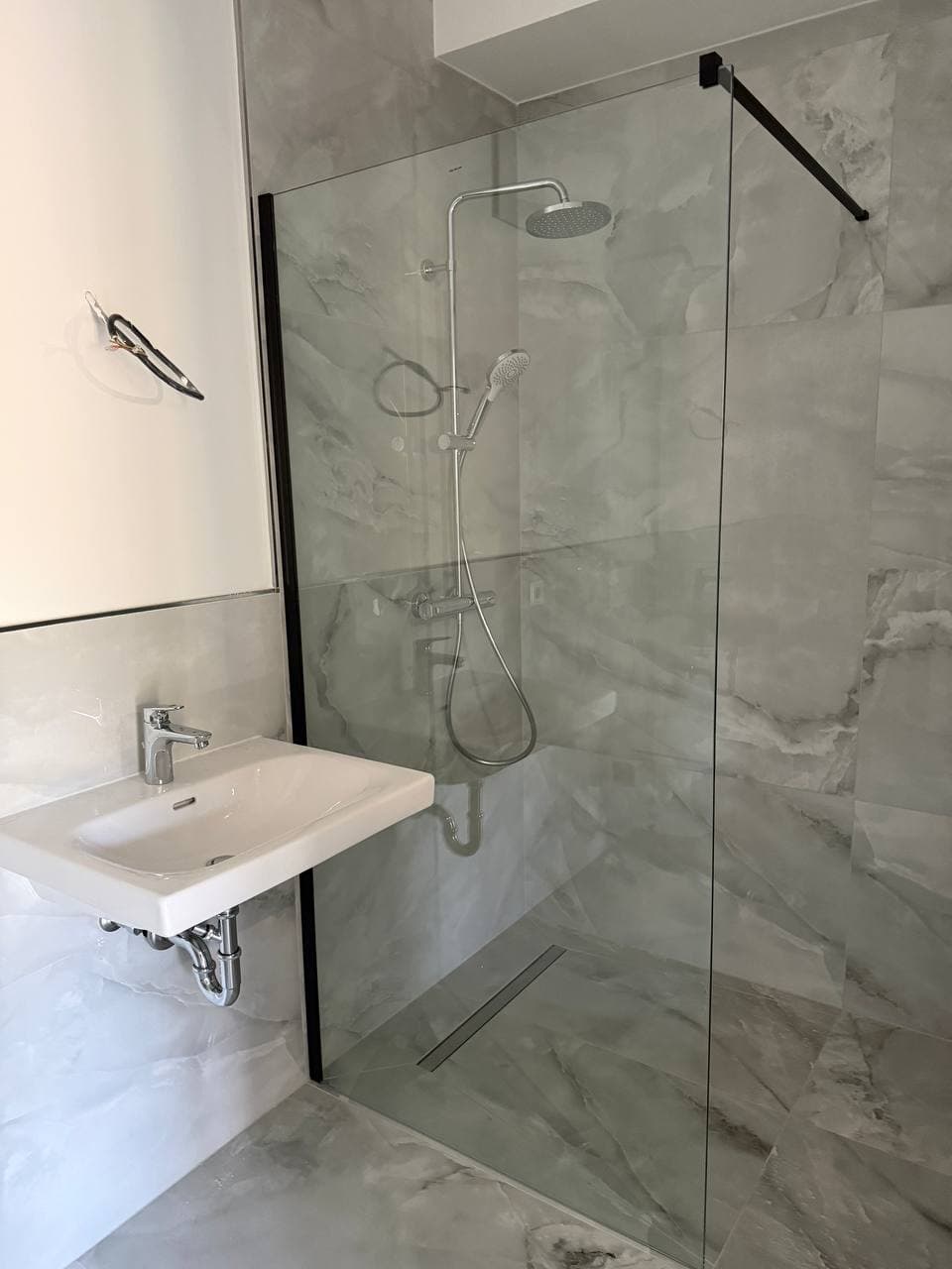 Bodengleiche Dusche mit schwarz gerahmter Glaswand, Regenbrause und Duschrinne, Wände in grauer Marmoroptik