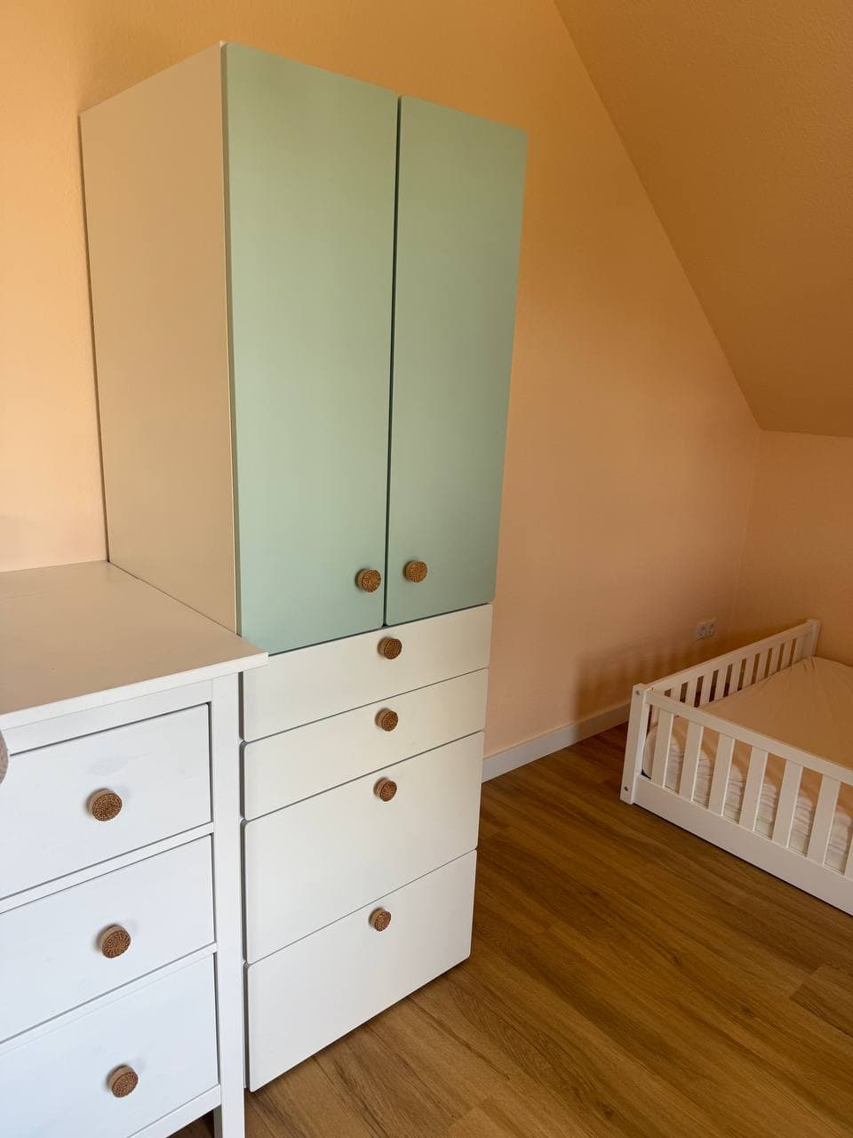 Kinderzimmer mit Dachschräge: Kleiderschrank mit mintgrünen Türen und weißen Schubladen, daneben eine weiße Kommode