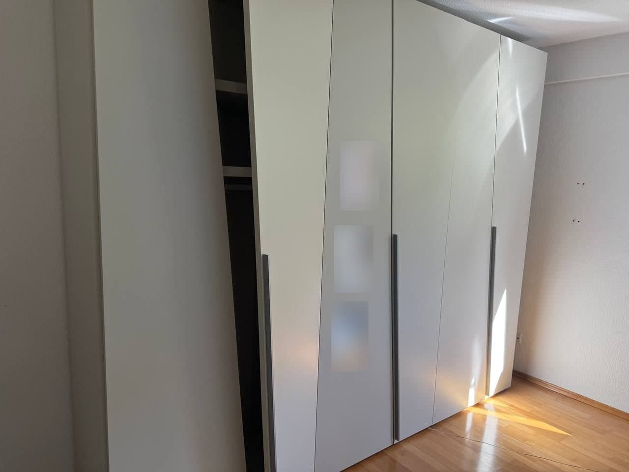 Breiter weißer Drehtürenschrank mit langen Griffleisten und drei kleinen Spiegeleinsätzen