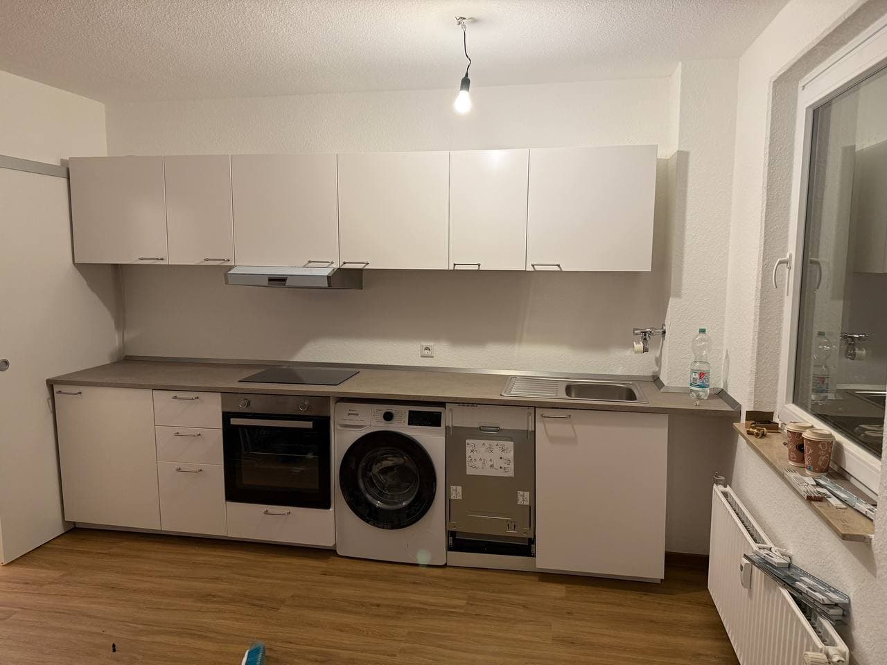 Weiße Küchenzeile mit Flachschirmhaube, Kochfeld, Einbaubackofen, Edelstahlspüle, Waschmaschine und Geschirrspüler