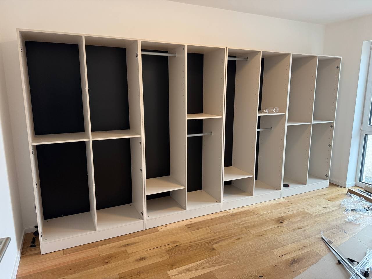 Große Schrankwand während des Aufbaus: helle Korpusse mit dunkler Rückwand, Kleiderstangen und Einlegeböden, noch ohne Türen